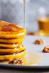 Yellow pancakes with corn flour and turmeric, dressed honey and red grapes. Healthy breakfast with superfoods. Light background, hugge scandinavian style