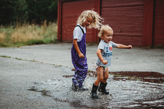 Siblings boy and girl jumping in a puddle having fun and smiling