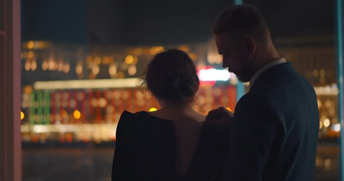 Back view of handsome man unzipping dress of beautiful woman standing together near panoramic window