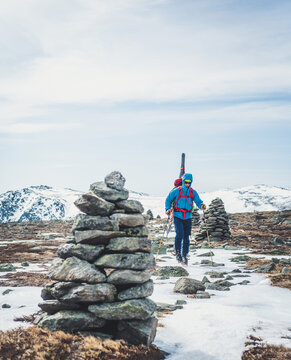 Man following cairns across snow and ice with skis on back