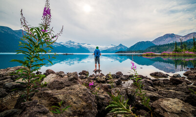 Male hiker standing on a rock overlooking a lake and snowy mountains