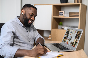 Fototapeta na wymiar Happy African American man using the app for distance video communication with coworkers, friends, meeting online, looking at the laptop screen with people profiles, studying, listening, making notes