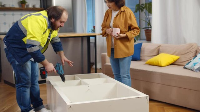 Handyman in uniform explaining senior woman how to assemble book shelf