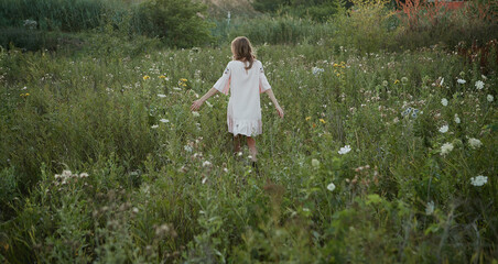 Blonde girl in pink linen dress walks in the field of flowers summer 