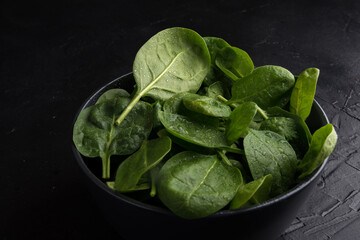 Baby spinach leaves with water drops in a ceramicn plate on a black background.