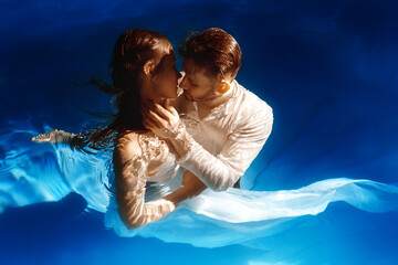 Couple kissing or hugging in the water. A girl in a dress with a long train and a guy are swimming...