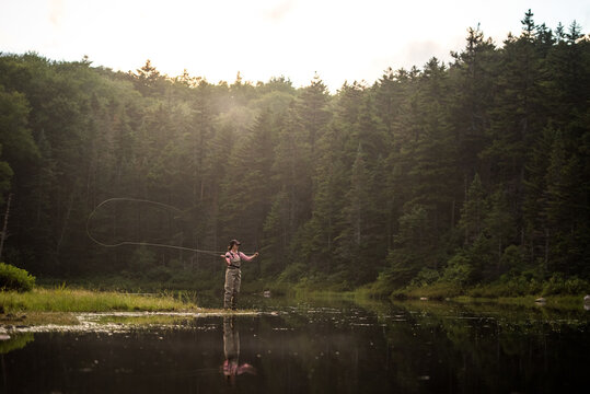 Woman angler fly-fishing in NH backcountry lake during afternoon light
