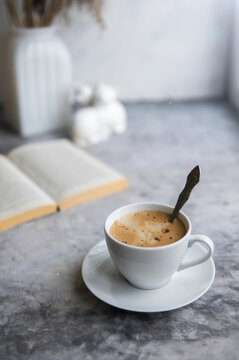 Breakfast on concrete table with open book and coffee cappuccino cup. Gray background, morning concept