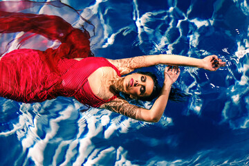 young woman in a red dress on the water. Girl swims in the water in a dress with a long train
