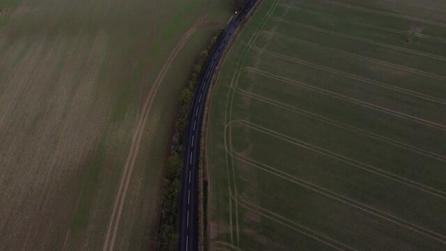 A drone reveal shot showing a beautiful country road with greenfields and open space