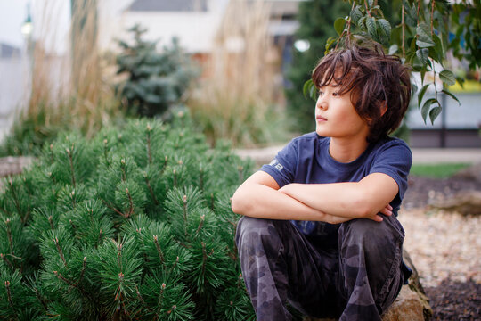 portrait of a beautiful boy sitting outside with a faraway look