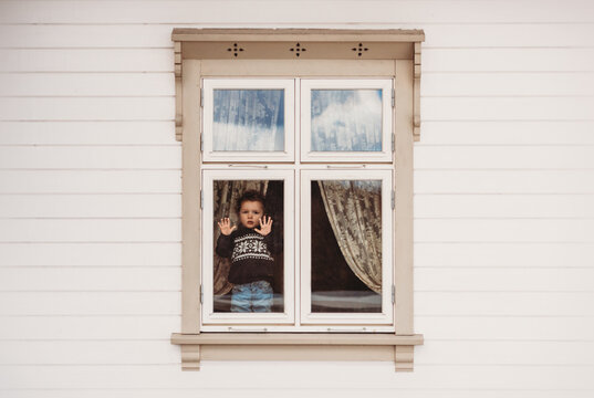 Little boy standing on window frame stuck at home in quarantine covid