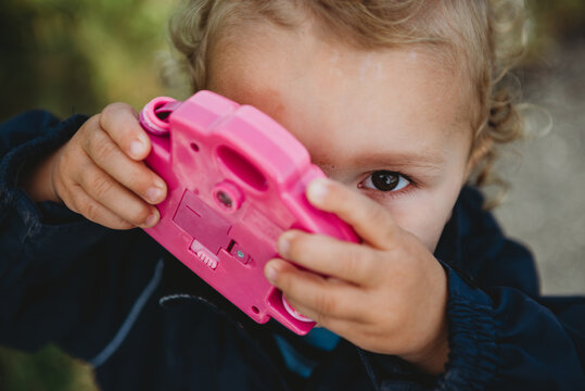 Young child holding a toy camera covering one eye looking up