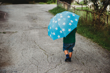 Back view of a child with an umbrella walking barefoot in the street