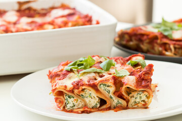 Freshly cooked cannelloni pasta filled with spinach and ricotta, served on white plate with fresh...