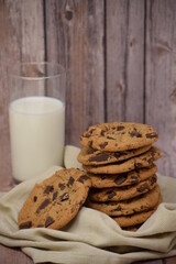 A stack of homemade chocolate chip cookies on a dishtowel with a glass of milk