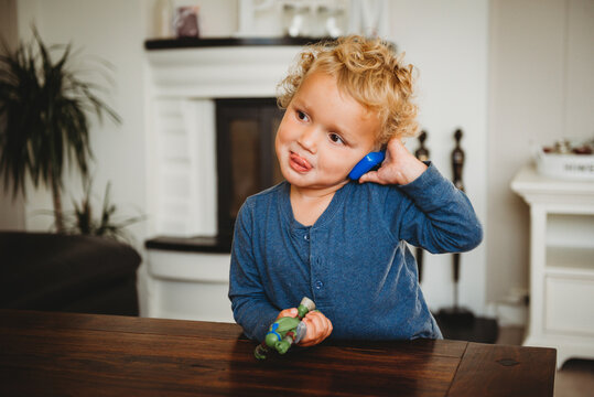 Adorable blonde boy pretending to speak on toy phone with tongue out