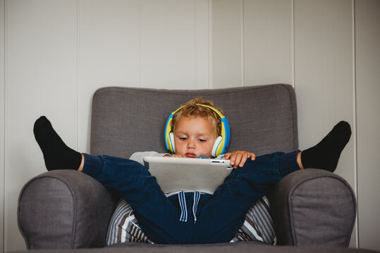 Child inside during isolation playing with tablet feet up on couch