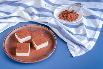 Still life with square souffle bird milk sprinkled with cocoa on a blue background top view