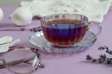 A cup of fragrant tea with lavender branches, glasses for vision against the background of needlework and white yarn, close-up