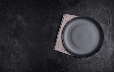 Black plate, linen napkin on black stone table top view. Table setting. - 409088901