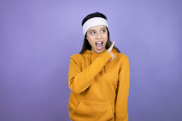 Young latin woman wearing sportswear over purple background smiling and pointing with hand and finger to the side