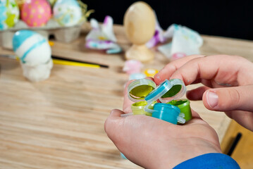 The boy paints an Easter egg. Paint in hand close up.