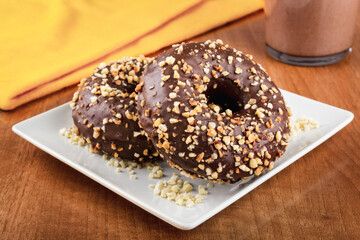 Delicious chocolate donuts covered with almond pieces on a white plate on a wooden table and accompanied by a glass of milk with cocoa