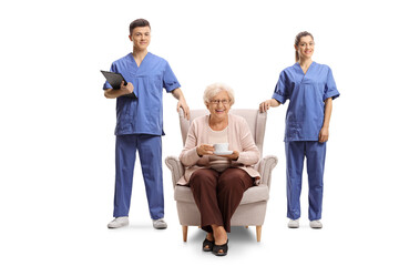 Male and female nurse standing next to an elderly woman seated in an armchair
