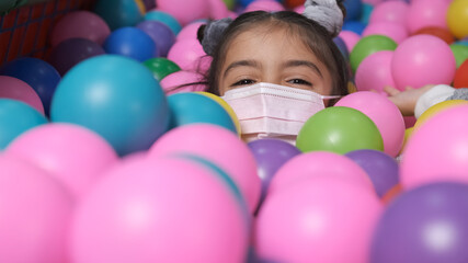 Fototapeta na wymiar happy 5 year old girl with mask in a ball pool throwing balls to camera