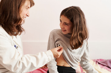 Female doctor teaching the temperature on a thermometer to a girl in her bed. Home doctor concept