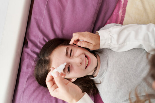 Top view of detail of female doctor smiling and giving eye drops to a little girl in her bed. Home doctor concept