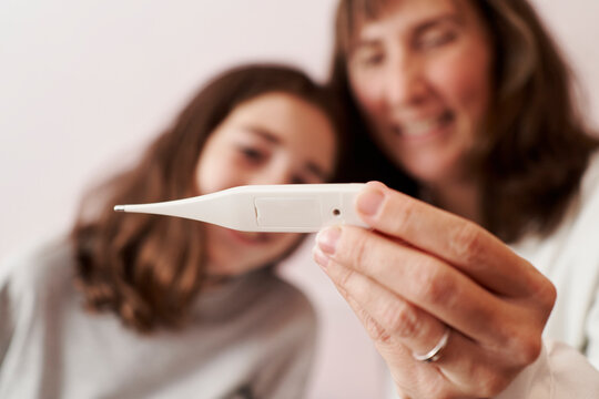 Female doctor teaching the temperature on a thermometer to a girl in her bed. Home doctor concept
