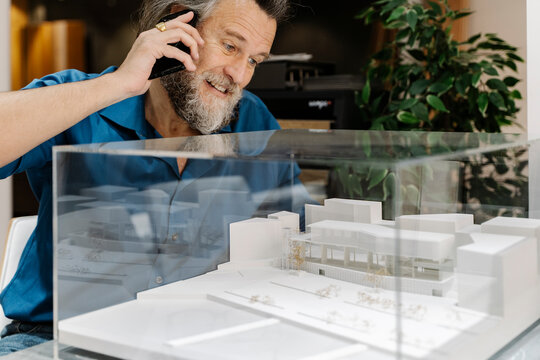 Mature man with a beard talking on the phone and looking at a model of