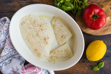 Raw halibut fish fillet, tomato, lemon basil and spices. White casserole on wooden rustic table, top view - 409092399