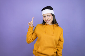 Young latin woman wearing sportswear over purple background showing and pointing up with fingers number one while smiling confident and happy