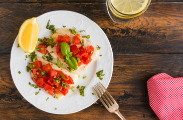 Halibut fish fillet baked with tomatoes. White plate, lemon, green basil, top view, close-up - 409092512