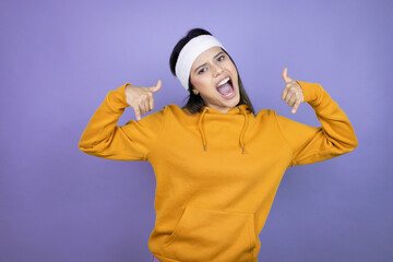 Young latin woman wearing sportswear over purple background shouting with crazy expression doing rock symbol with hands up