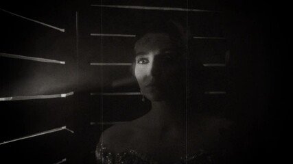 Mysterious young beautiful sad fright retro woman stands in dark fear night room. Black white film style 30s. Backdrop creative bright light moves breaks through cracks openings screen. Stylized party