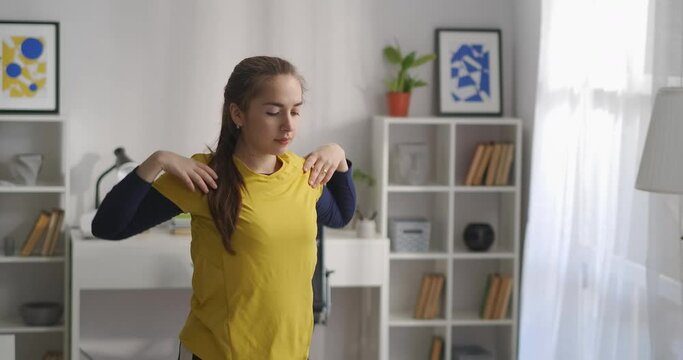 young woman is doing exercises for shoulders and neck, warming muscles at morning workout, rotating arms forward and back