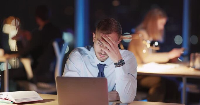 Young overworked caucasian executive performing project in laptop worrying about deadlines. Procrastination concept. Night office.
