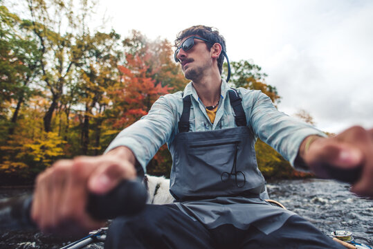 Fly fisherman rowing boat down river in fall foliage season
