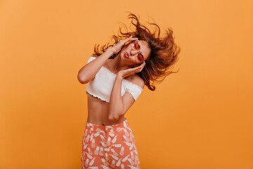 Attractive woman of 22 years old is dancing and listening to music with her eyes closed. Shot in studio of pretty girl in pink glasses and white cropped t-shirt