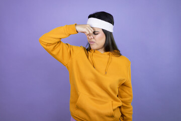 Young latin woman wearing sportswear over purple background smelling something stinky and disgusting, intolerable smell, holding breath with fingers on nose