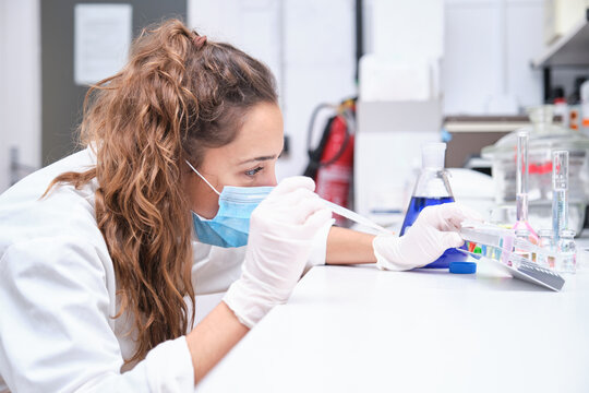 Young female scientist using a Pasteur pipette and a rack with tubes. Laboratory research concept.