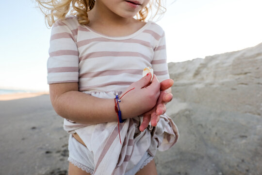 detail shot of little girl holding shells on the beach with dress on