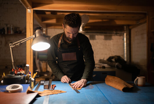 Bearded craftsman measuring leather in workshop
