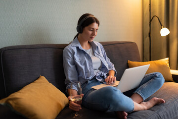 Young woman drinking wine and watching film on laptop at home