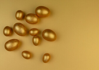 Decorative wooden Easter eggs painted gold on yellow-gold background. Happy Easter greeting card.