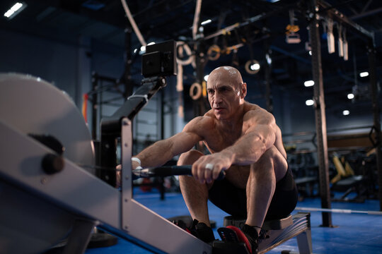 Tough Senior Sportsman Doing Rowing Exercise In Gym